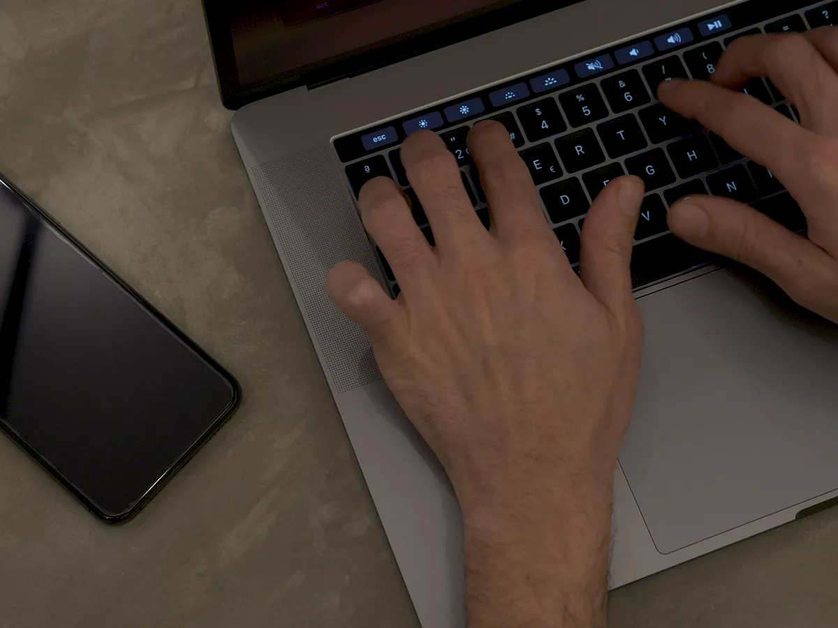 Hands working on a laptop next to a phone